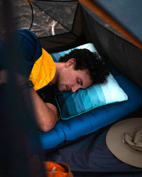 A man sleeping in a tent using the Rumpl Adjustable Camp Pillow