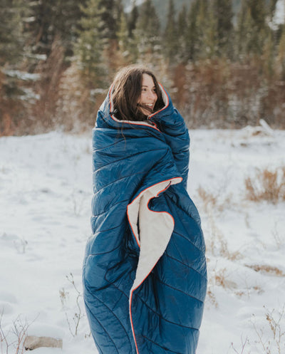 A woman stands outside in the snow, all bundled up in one of the ultra-soft Rumpl Sherpa Blankets.