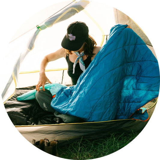 A woman sitting in a tent takes a Rumpl camping blanket out of its stuff sack